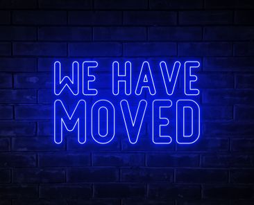 We have moved - blue neon light word on brick wall background